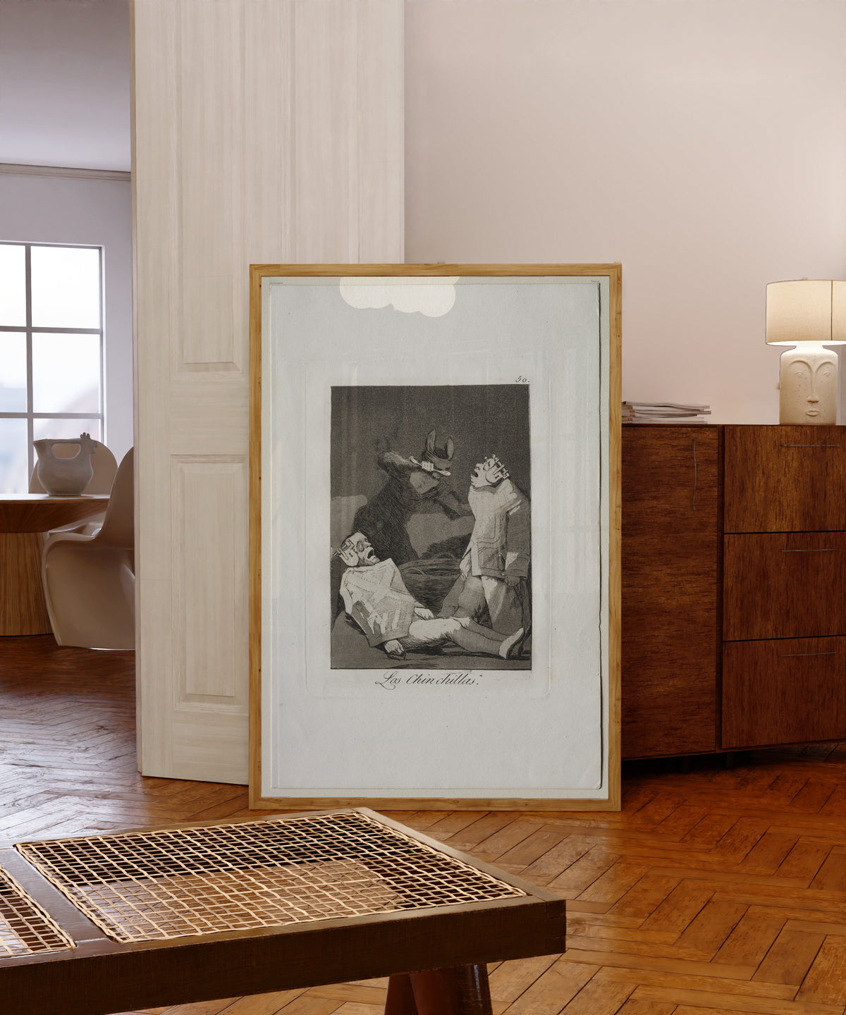 Framed art print of Las Chinchillas, Los Caprichos, Plate 50 by Francisco de Goya, in a light wood frame leaning in a warm room with a parquet floor