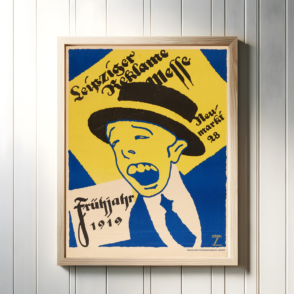 Framed art print of Leipziger Reklame-Messe, Frühjahr 1919 by Ludwig Hohlwein, in a light wood frame on a white panelled wall