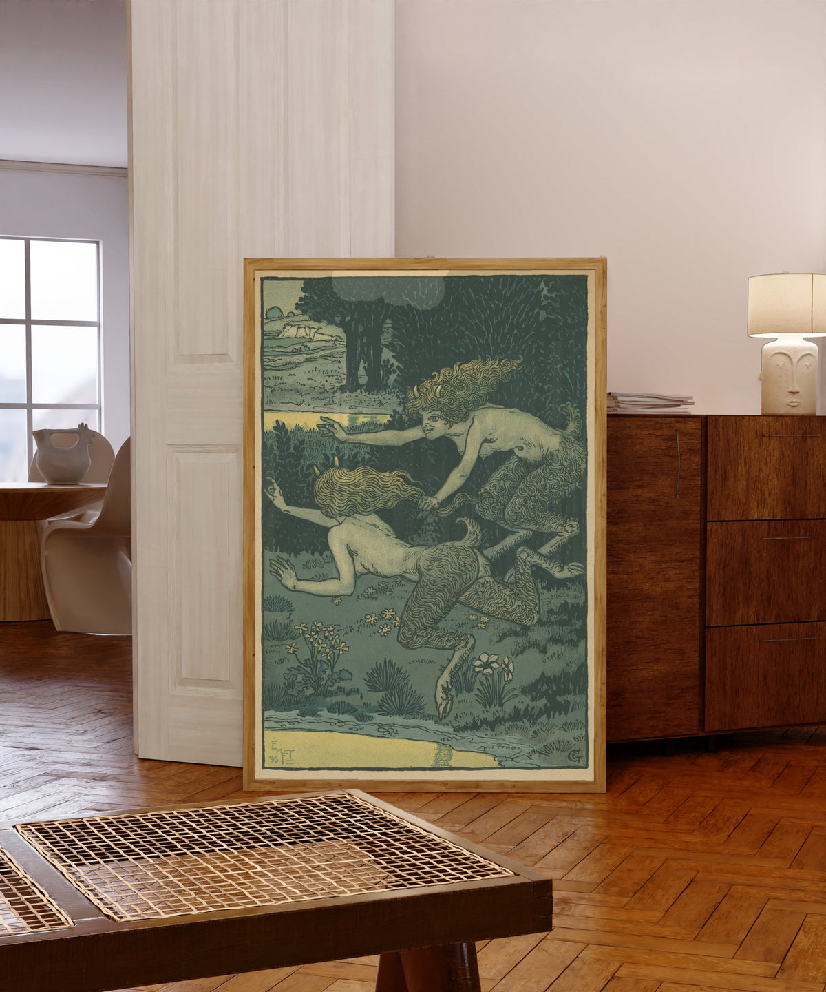 Framed art print of Les petites faunesses by Eugène Grasset, in a light wood frame leaning in a warm room with a parquet floor