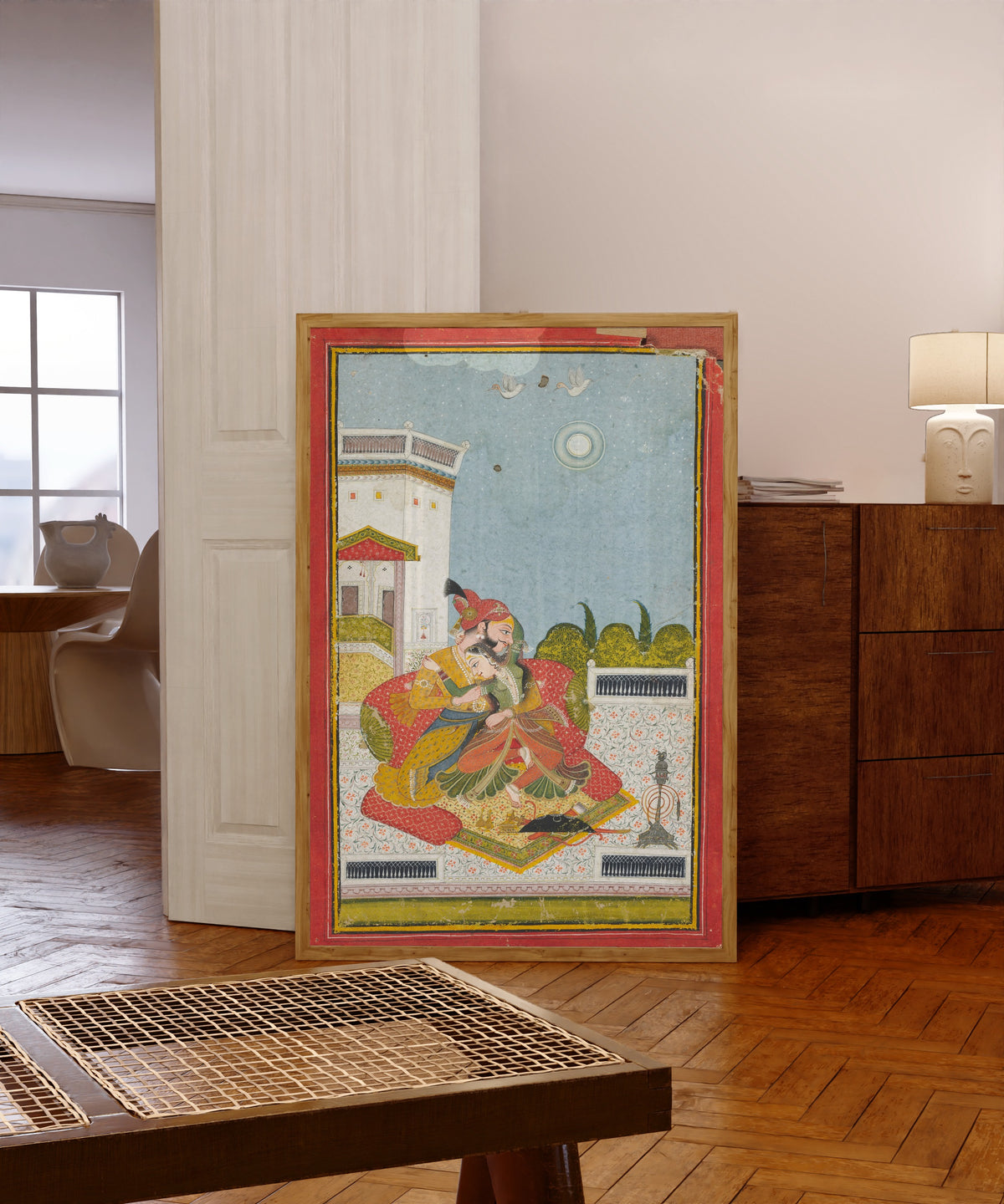 Framed art print of Lovers Embracing (Raga Malkaus) by Bundi school, in a light wood frame leaning in a warm room with a parquet floor