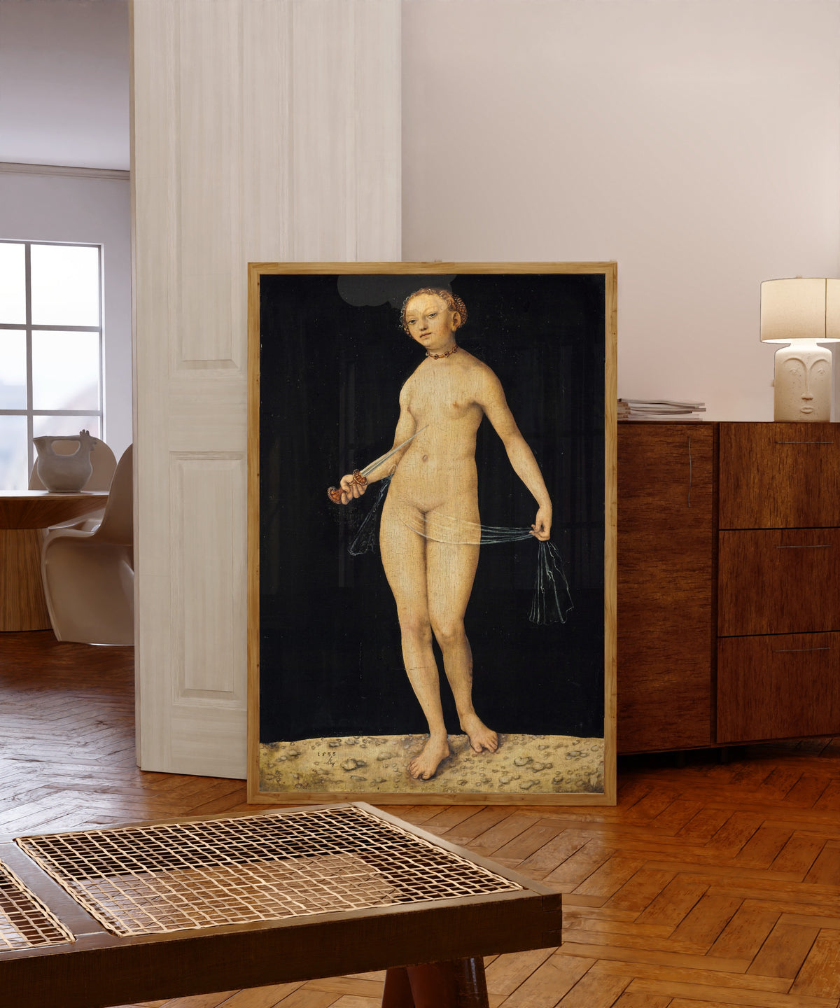 Framed art print of Lucretia by Lucas Cranach the Elder, in a light wood frame leaning in a warm room with a parquet floor