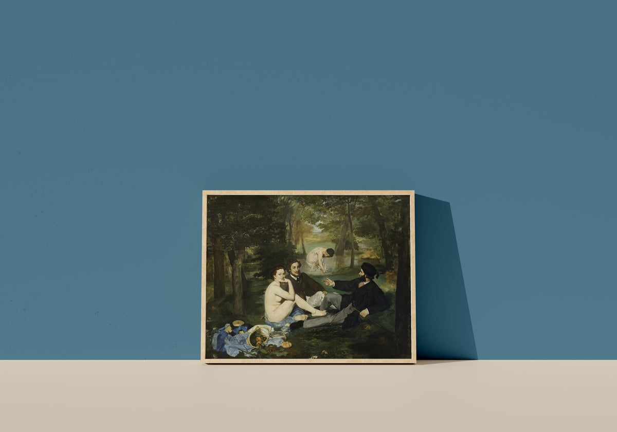 Framed art print of Luncheon on the Grass by Édouard Manet, in a light wood frame leaning on a blue wall