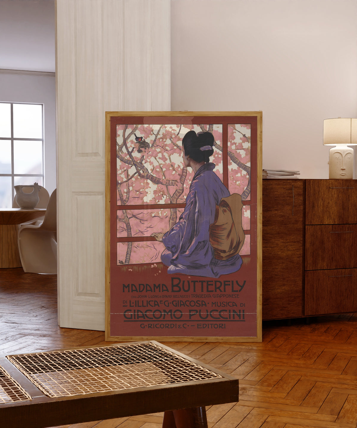 Framed art print of Madama Butterfly: Tragedia giapponese by Leopoldo Metlicovitz, in a light wood frame leaning in a warm room with a parquet floor