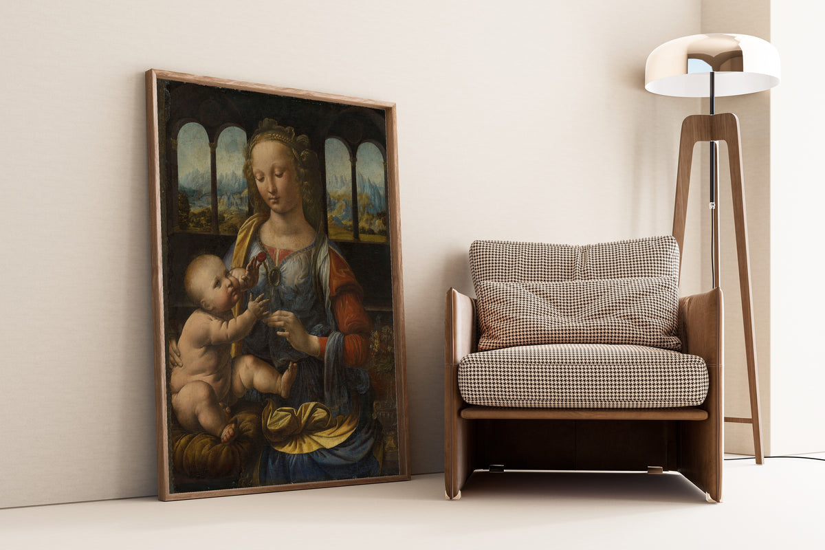Framed art print of Madonna of the Carnation by Leonardo da Vinci, leaning against a wall beside an armchair and a floor lamp