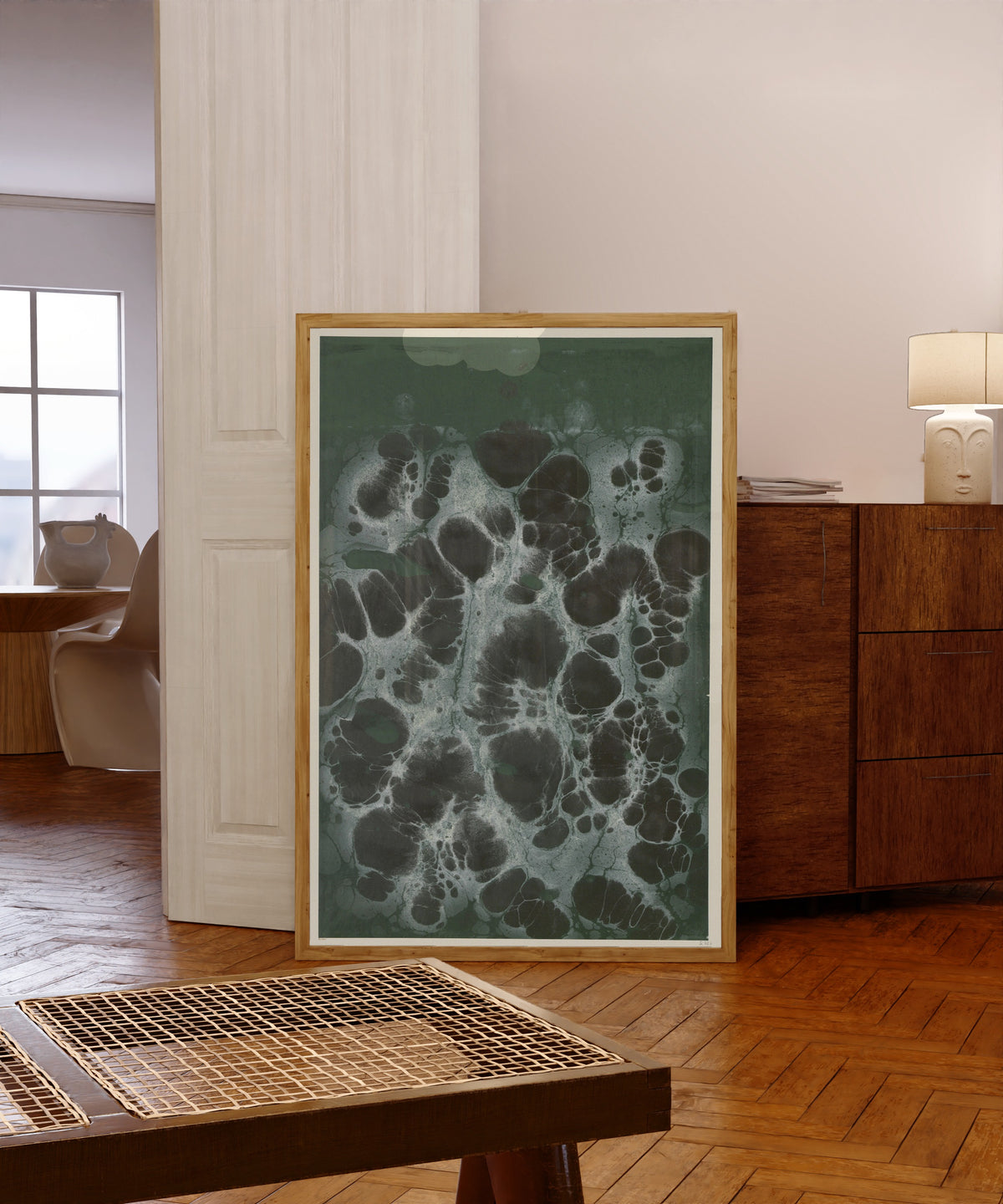 Framed art print of Marmorpapier (black cells on dark green) by Otto Eckmann, in a light wood frame leaning in a warm room with a parquet floor