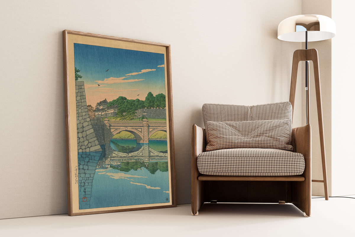 Framed art print of Morning at Nijū Bridge by Kawase Hasui, leaning against a wall beside an armchair and a floor lamp