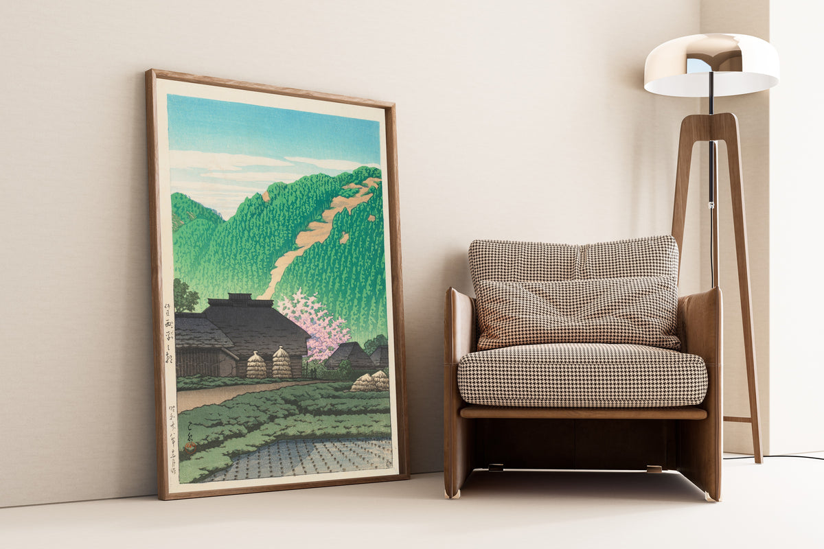 Framed art print of Morning in Nishibira, Izu by Kawase Hasui, leaning against a wall beside an armchair and a floor lamp