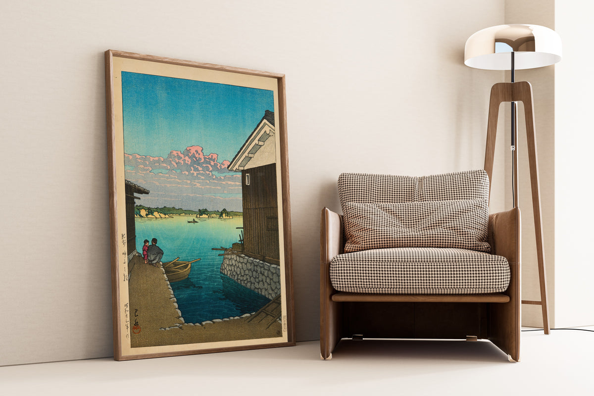 Framed art print of Morning in Yobuko, Hizen by Kawase Hasui, leaning against a wall beside an armchair and a floor lamp
