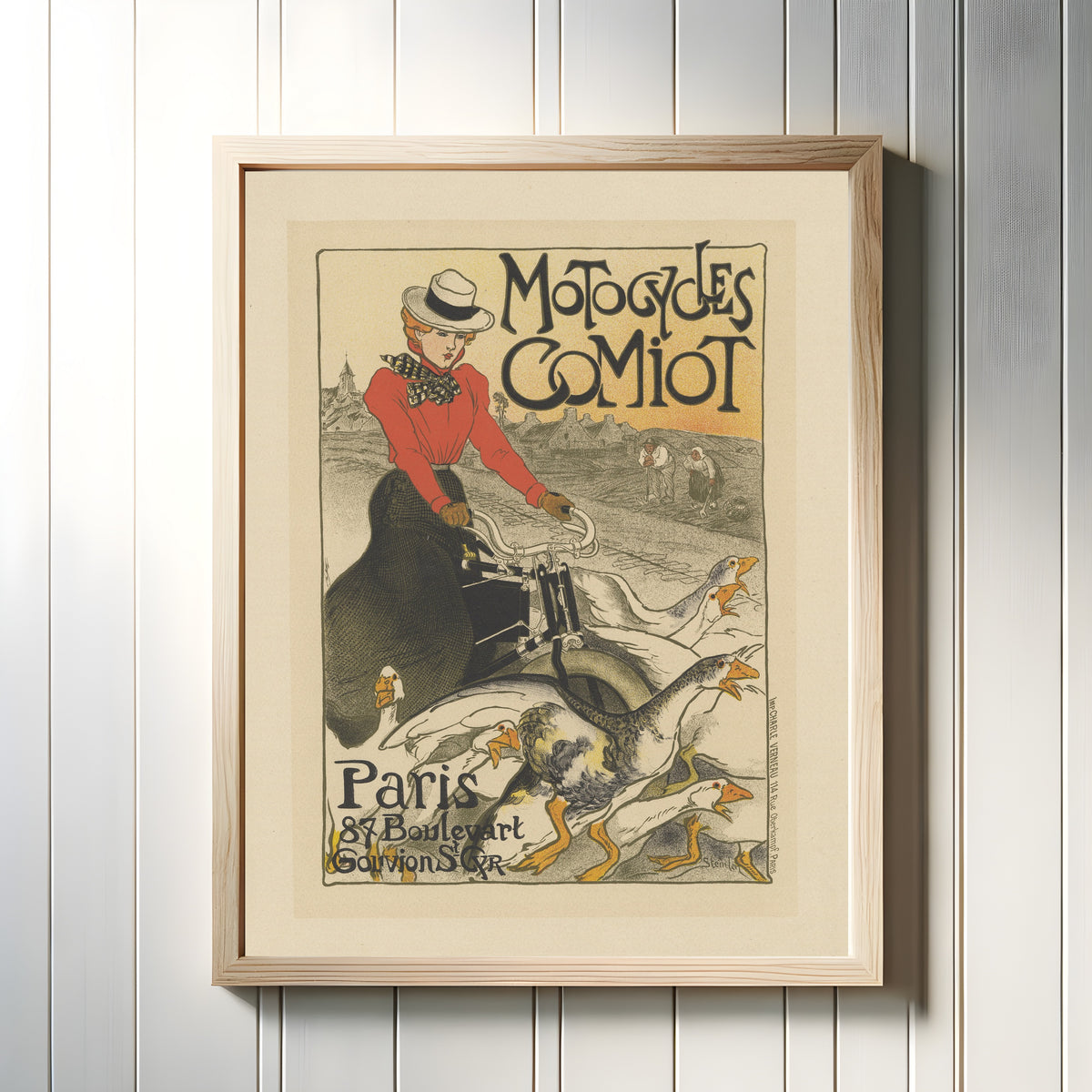 Framed art print of Motocycles Comiot, Paris by Théophile Steinlen, in a light wood frame on a white panelled wall