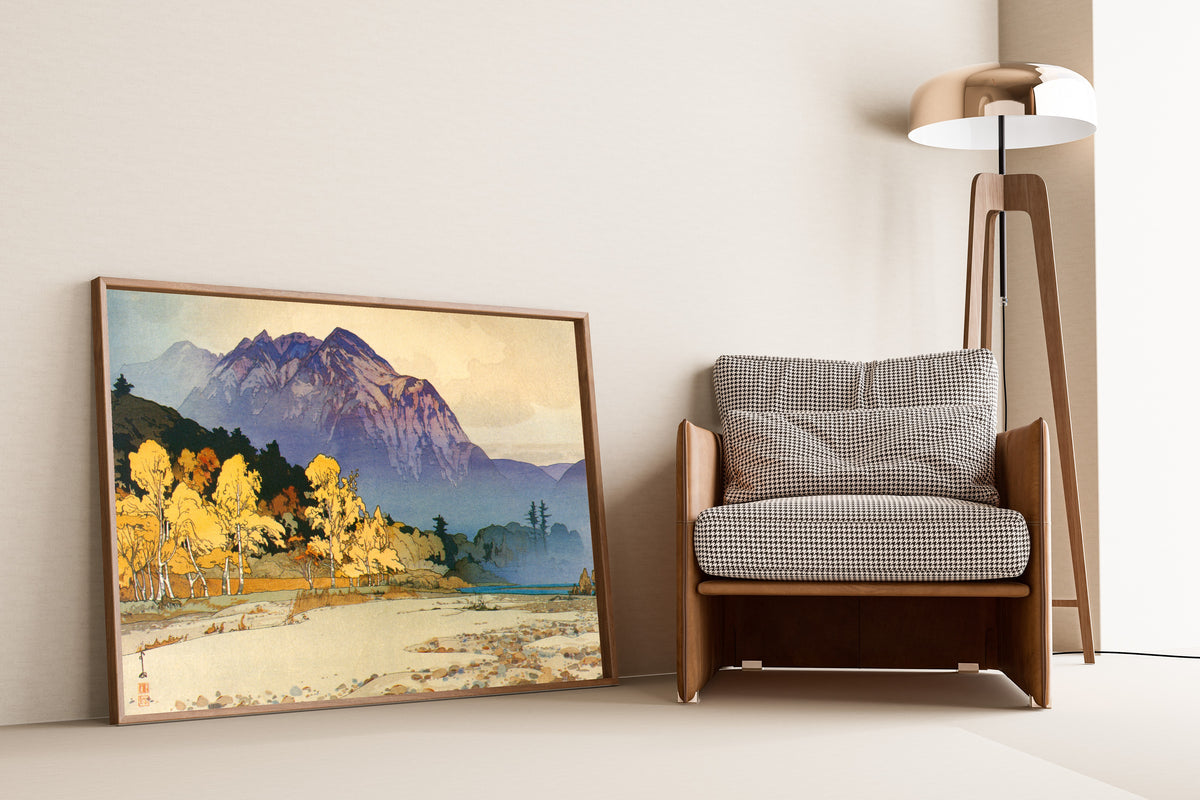 Framed art print of Mount Hodaka after Rain by Hiroshi Yoshida, leaning against a wall beside an armchair and a floor lamp