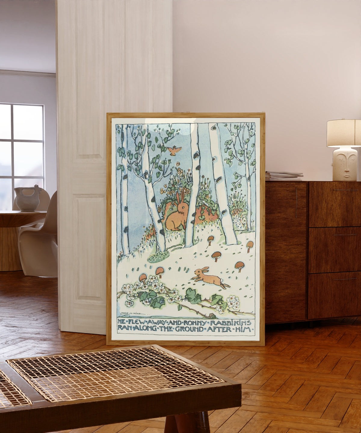 Framed art print of Mummy's Bedtime Story Book: He Flew Away and Ronny… by Jessie M. King, in a light wood frame leaning in a warm room with a parquet floor