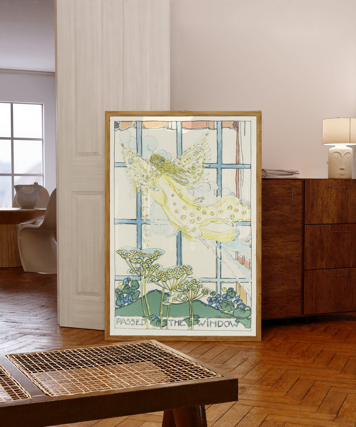 Framed art print of Mummy's Bedtime Story Book: Plate 6 by Jessie M. King, in a light wood frame leaning in a warm room with a parquet floor
