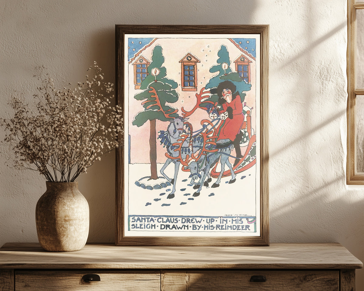 Framed art print of Mummy's Bedtime Story Book: Santa Claus Drew Up… by Jessie M. King, in a dark wood frame leaning on a rustic console beside dried flowers