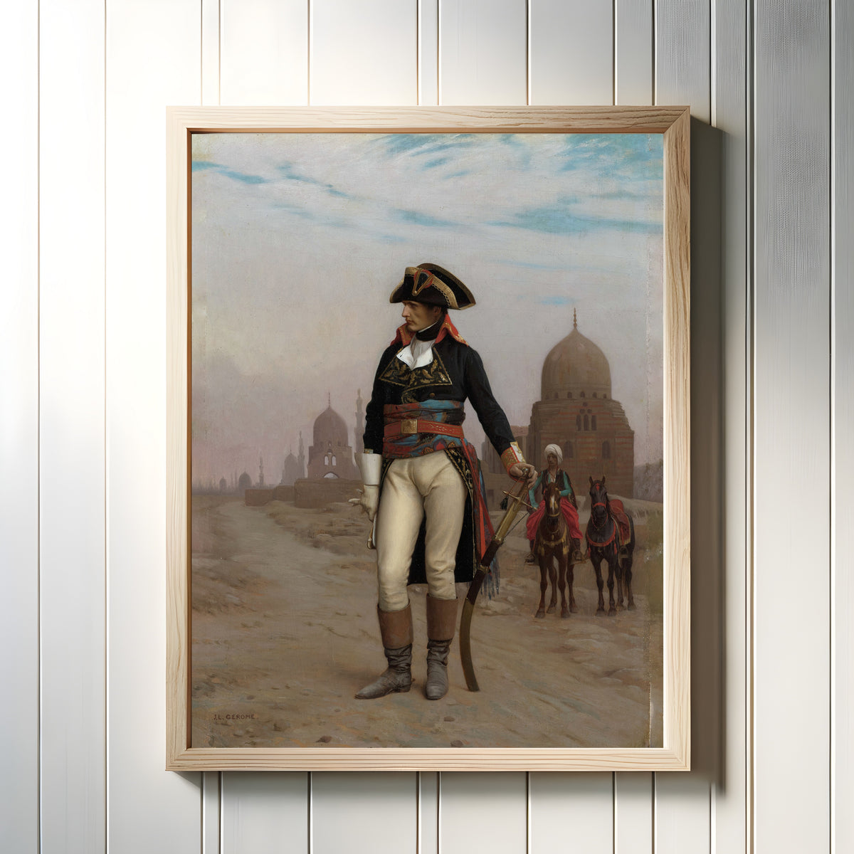 Framed art print of Napoleon in Egypt by Jean-Léon Gérôme, in a light wood frame on a white panelled wall