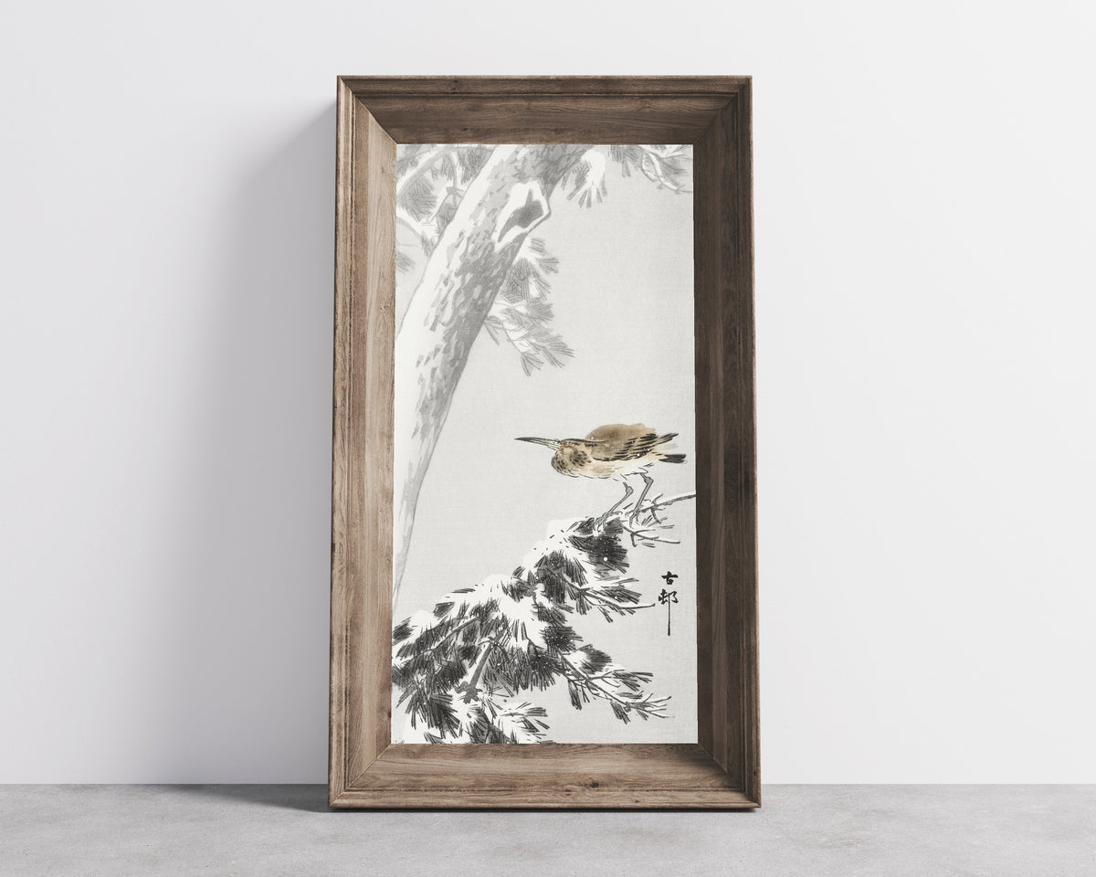 Framed art print of Night Heron on a Snowy Pine Branch by Ohara Koson, in a wide wooden frame leaning against a concrete wall