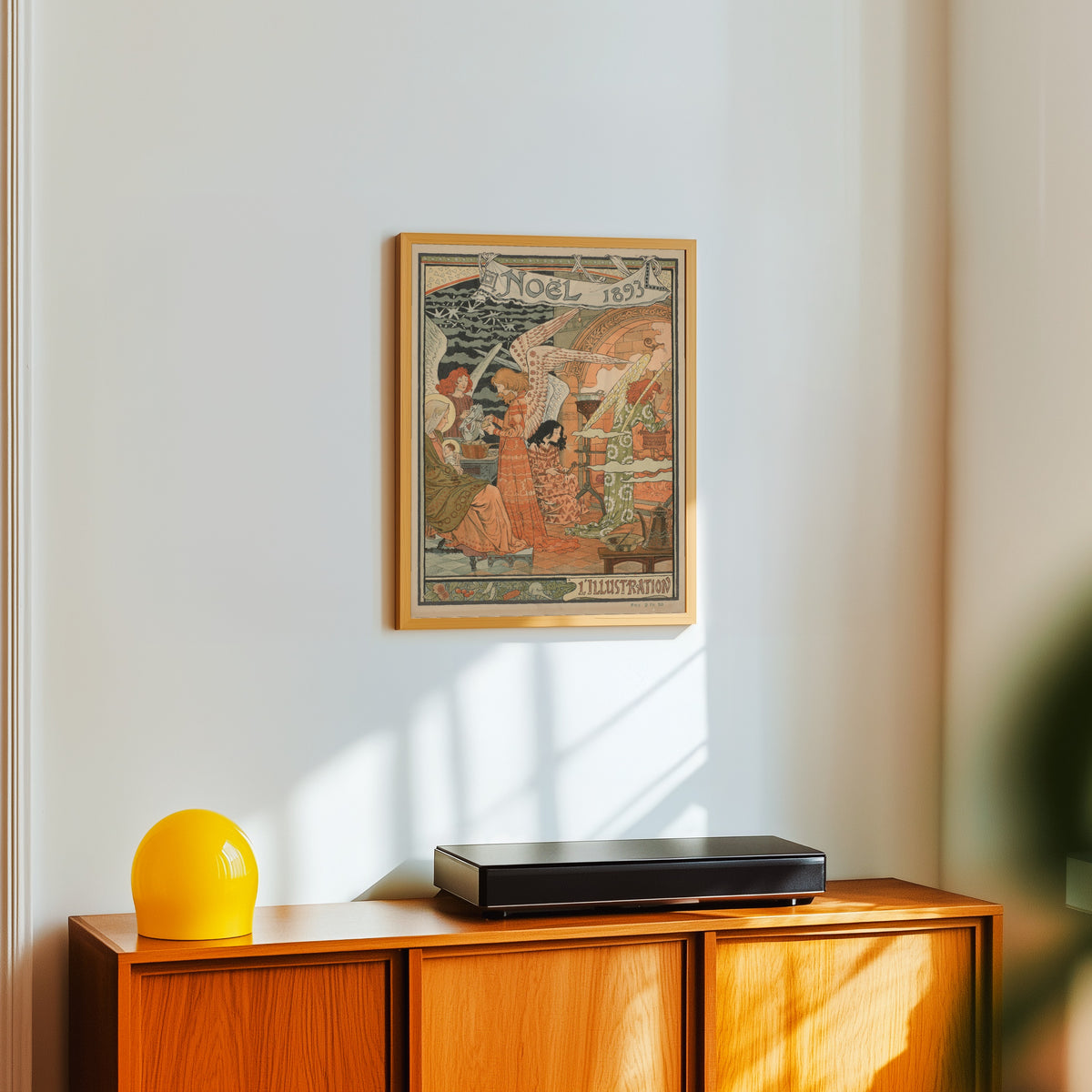 Framed art print of Noël 1893 by Eugène Grasset, in a light wood frame on a white wall above an orange sideboard