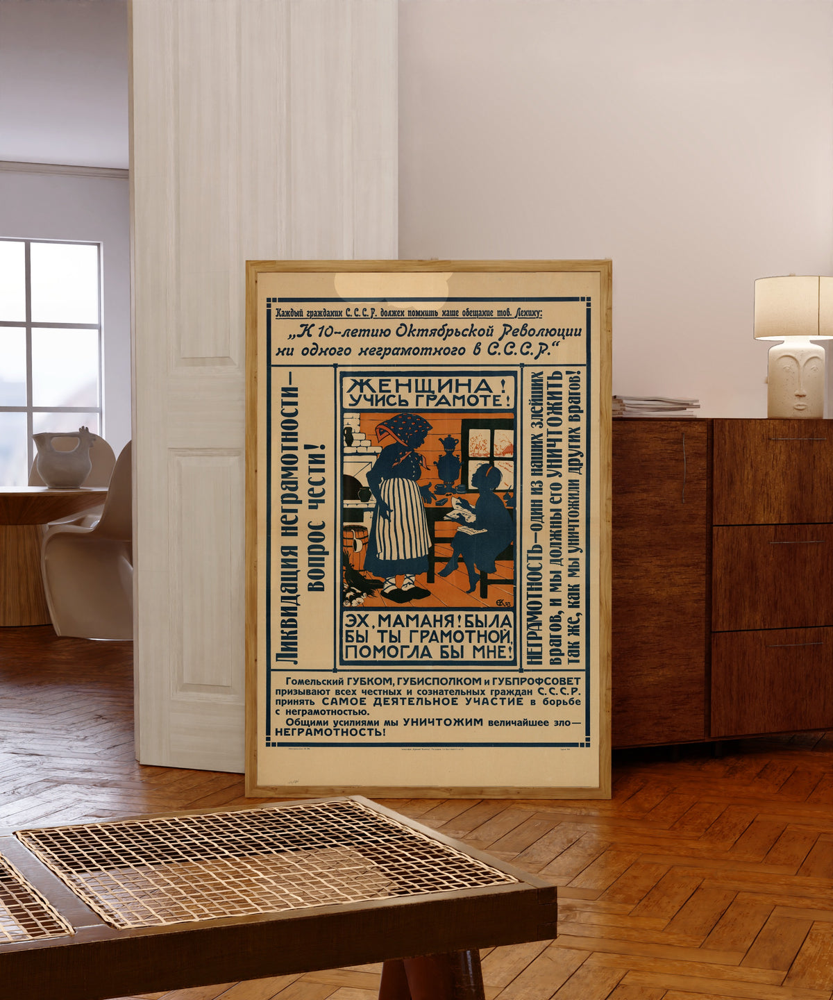 Framed art print of Not a Single Illiterate in the USSR by Elizaveta Kruglikova, in a light wood frame leaning in a warm room with a parquet floor