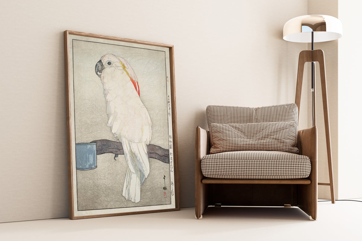 Framed art print of Obatan Parrot by Hiroshi Yoshida, leaning against a wall beside an armchair and a floor lamp