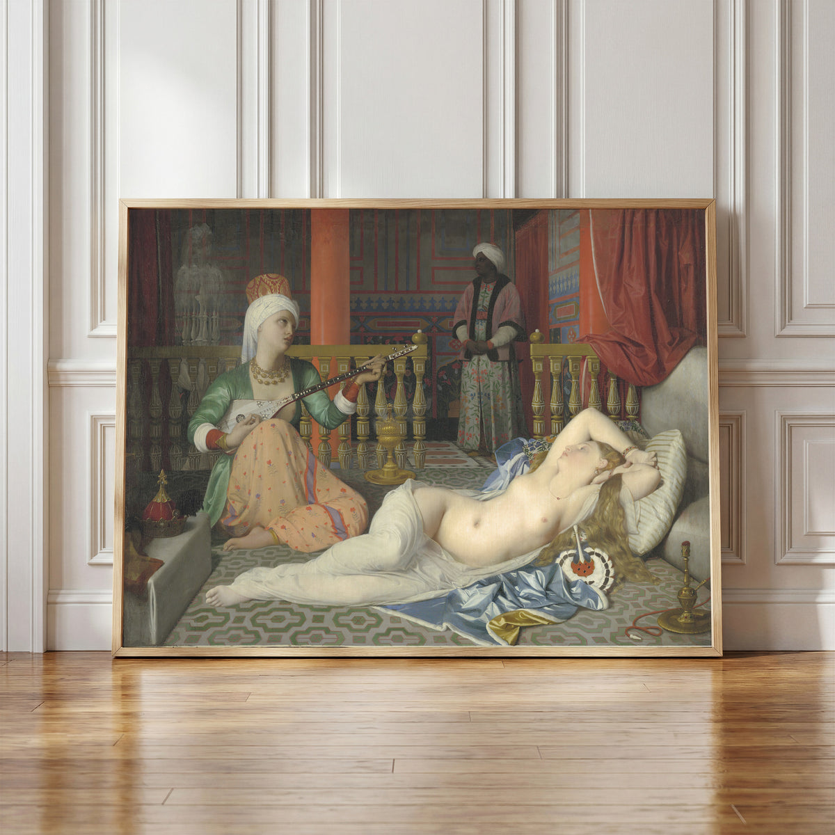 Framed art print of Odalisque with Slave by Jean-Auguste-Dominique Ingres, in a light wood frame leaning against a panelled white wall