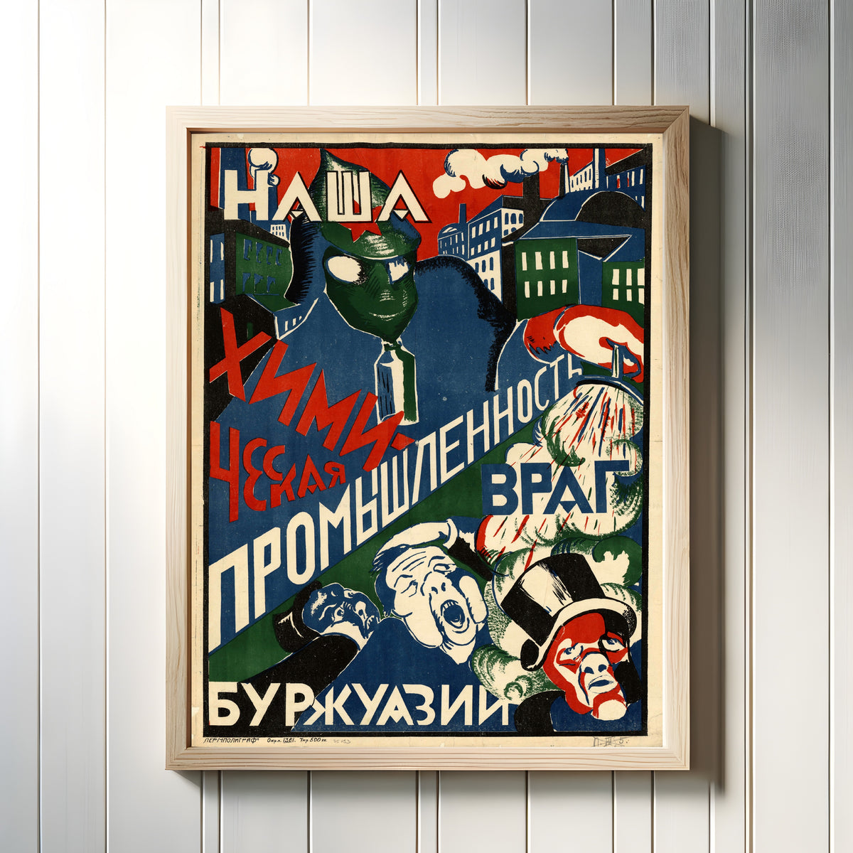 Framed art print of Our Chemical Industry Is the Enemy of the Bourgeoisie, in a light wood frame on a white panelled wall