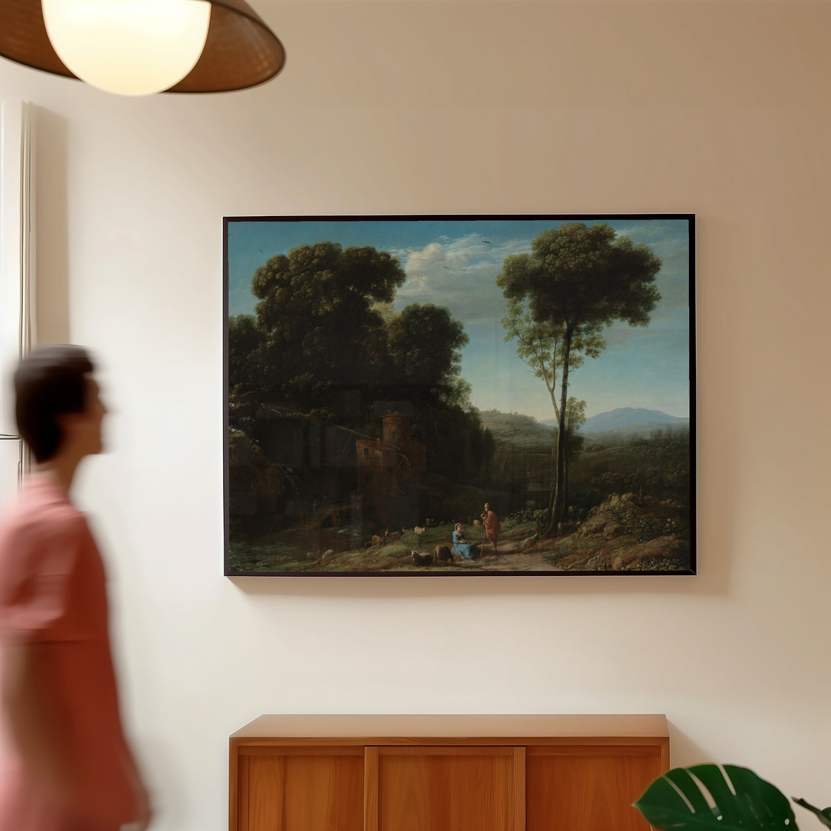 Framed art print of Pastoral Landscape with a Mill by Claude Lorrain, in a slim black frame on a warm wall in a sunlit room