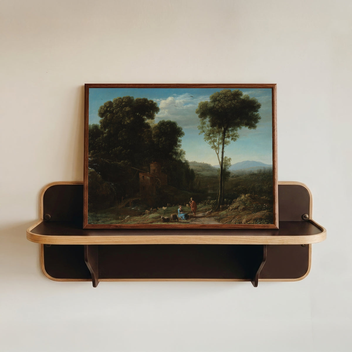 Framed art print of Pastoral Landscape with a Mill by Claude Lorrain, in a dark wood frame resting on a wall shelf