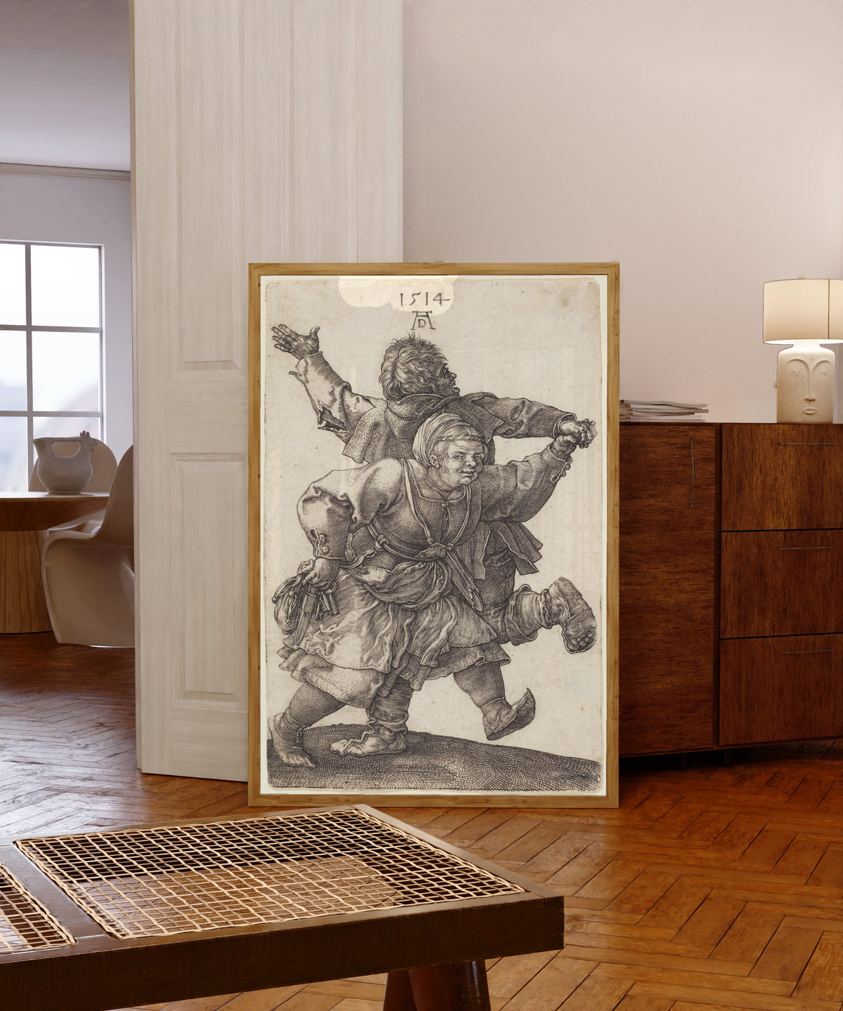 Framed art print of Peasant Couple Dancing by Albrecht Dürer, in a light wood frame leaning in a warm room with a parquet floor