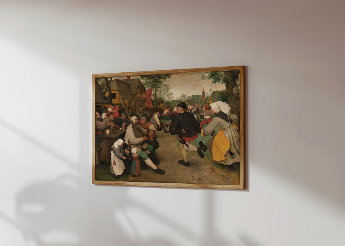Framed art print of Peasant Dance by Pieter Bruegel the Elder, in a light wood frame on a sunlit white wall, seen at a slight angle