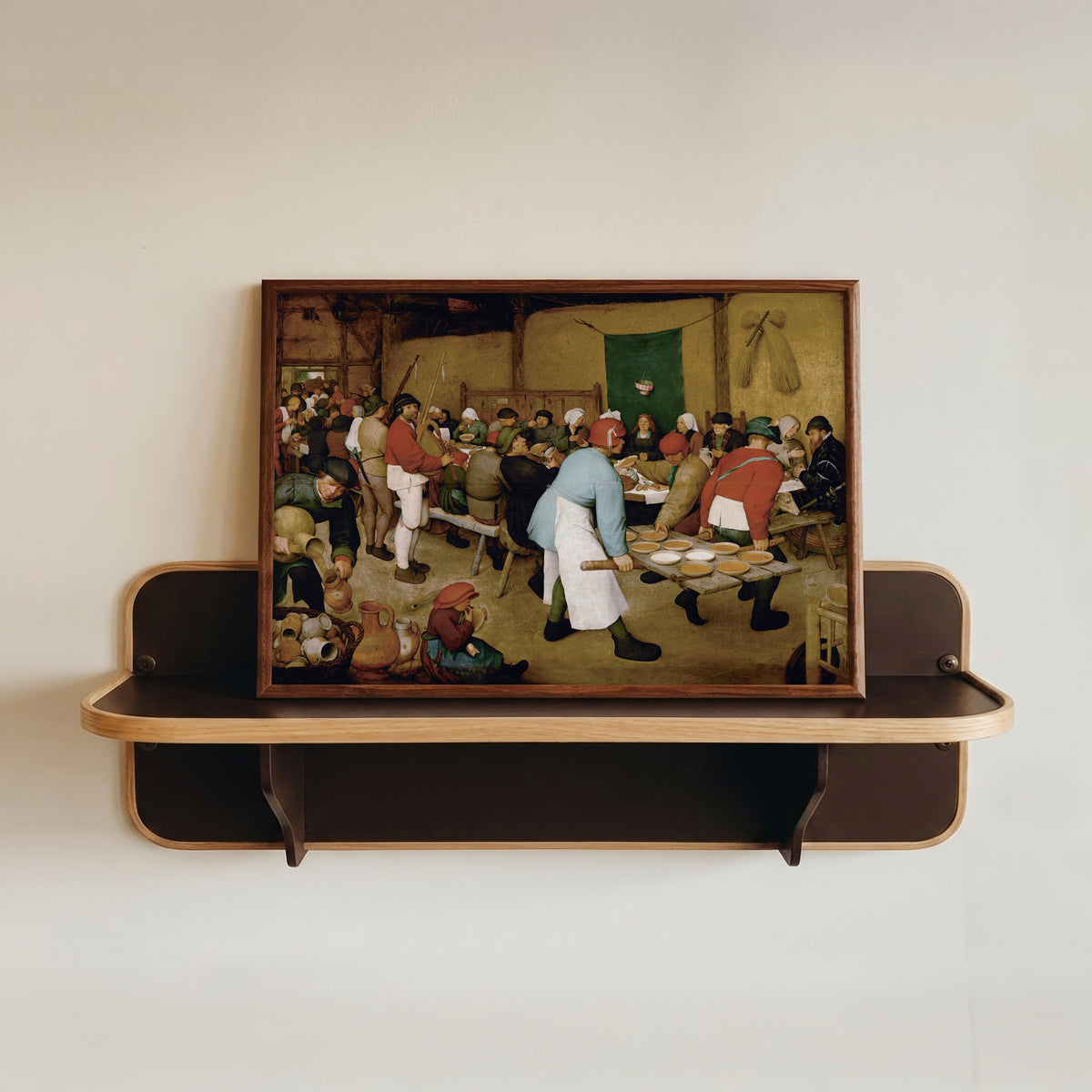 Framed art print of Peasant Wedding by Pieter Bruegel the Elder, in a dark wood frame resting on a wall shelf