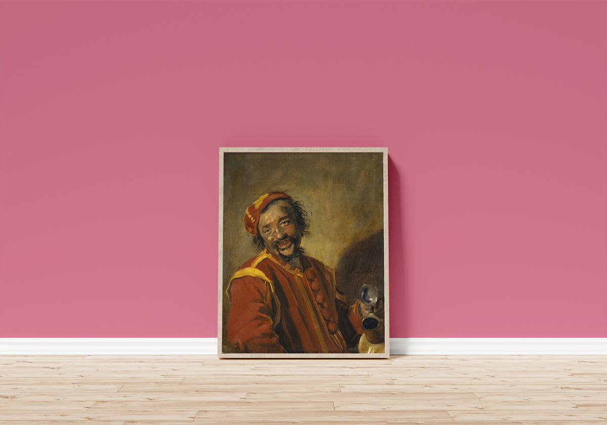 Framed art print of Peeckelhaering by Frans Hals, in a light wood frame leaning on a pink wall above a wooden floor