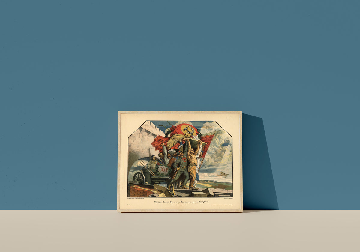 Framed art print of Peoples of the Union of Soviet Socialist Republics by Stepan Karpov, in a light wood frame leaning on a blue wall