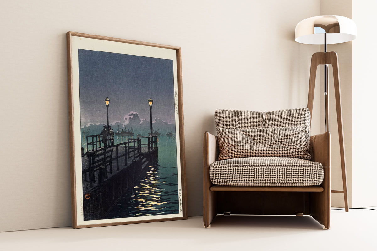 Framed art print of Pier at Otaru by Kawase Hasui, leaning against a wall beside an armchair and a floor lamp