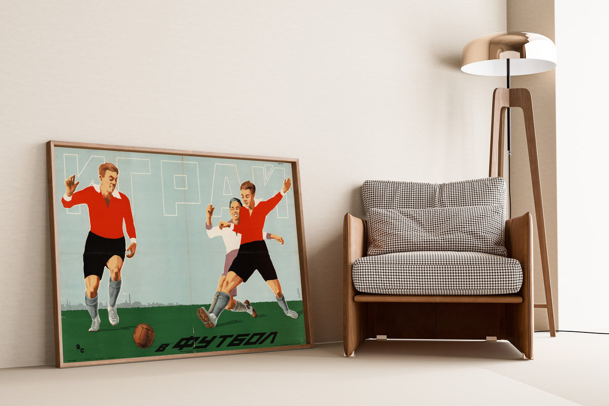 Framed art print of Play Football, leaning against a wall beside an armchair and a floor lamp