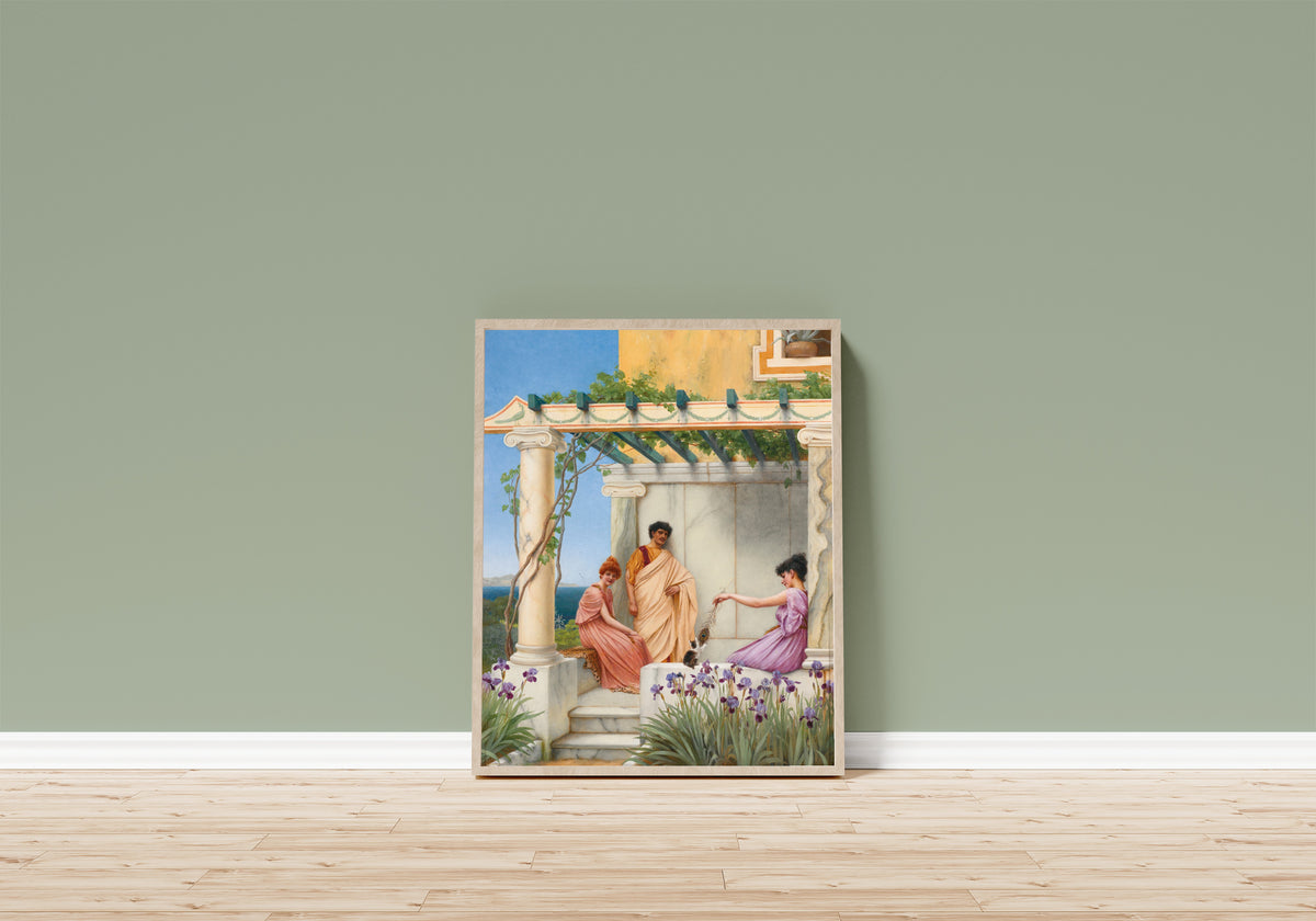 Framed art print of Playtime by John William Godward, in a light wood frame leaning on a sage green wall above a wooden floor