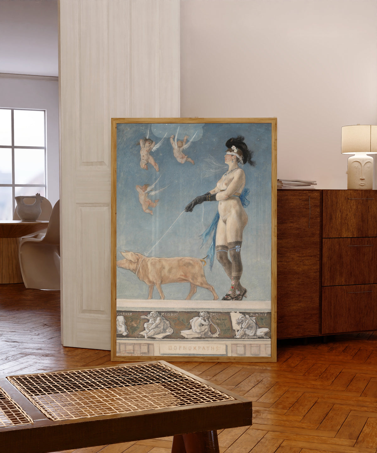 Framed art print of Pornokratès by Félicien Rops, in a light wood frame leaning in a warm room with a parquet floor