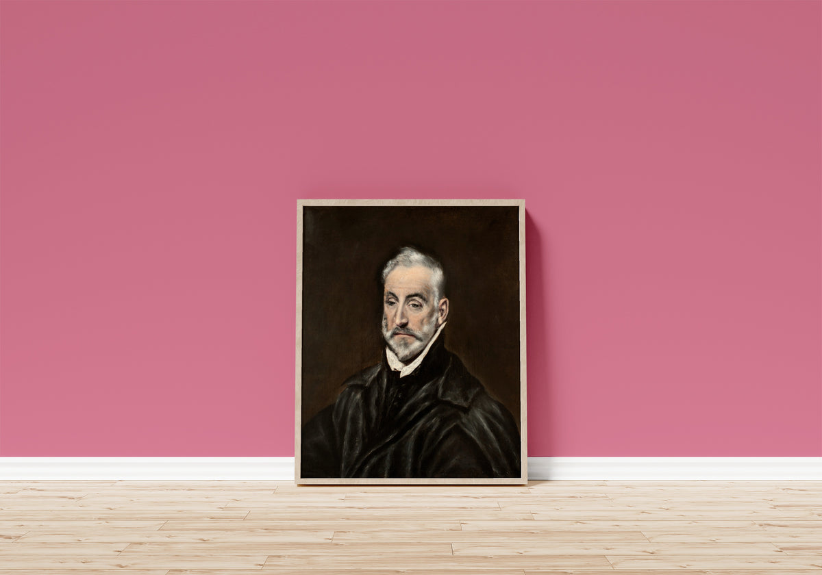 Framed art print of Portrait of Antonio de Covarrubias y Leiva by El Greco, in a light wood frame leaning on a pink wall above a wooden floor