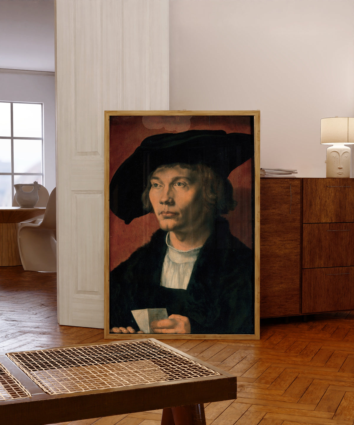 Framed art print of Portrait of Bernhart von Reesen by Albrecht Dürer, in a light wood frame leaning in a warm room with a parquet floor