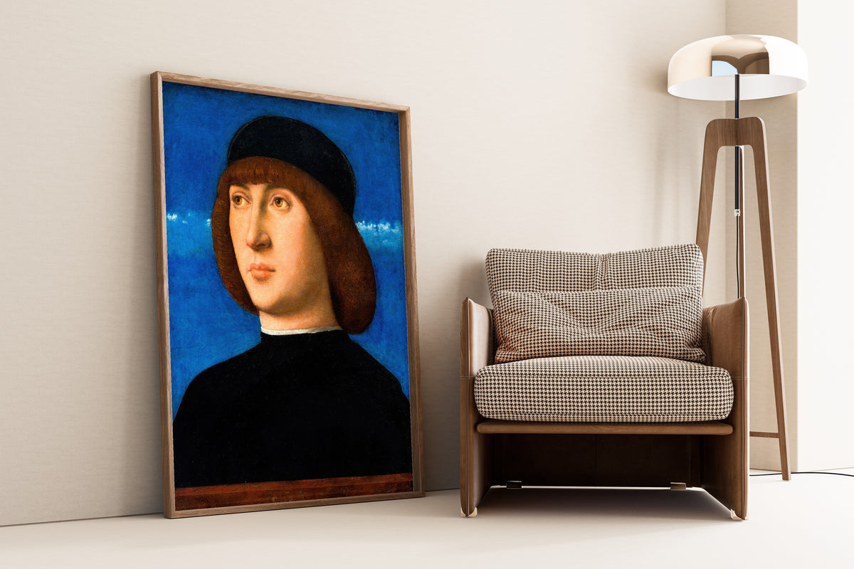 Framed art print of Portrait of a Young Man by Giovanni Bellini, leaning against a wall beside an armchair and a floor lamp