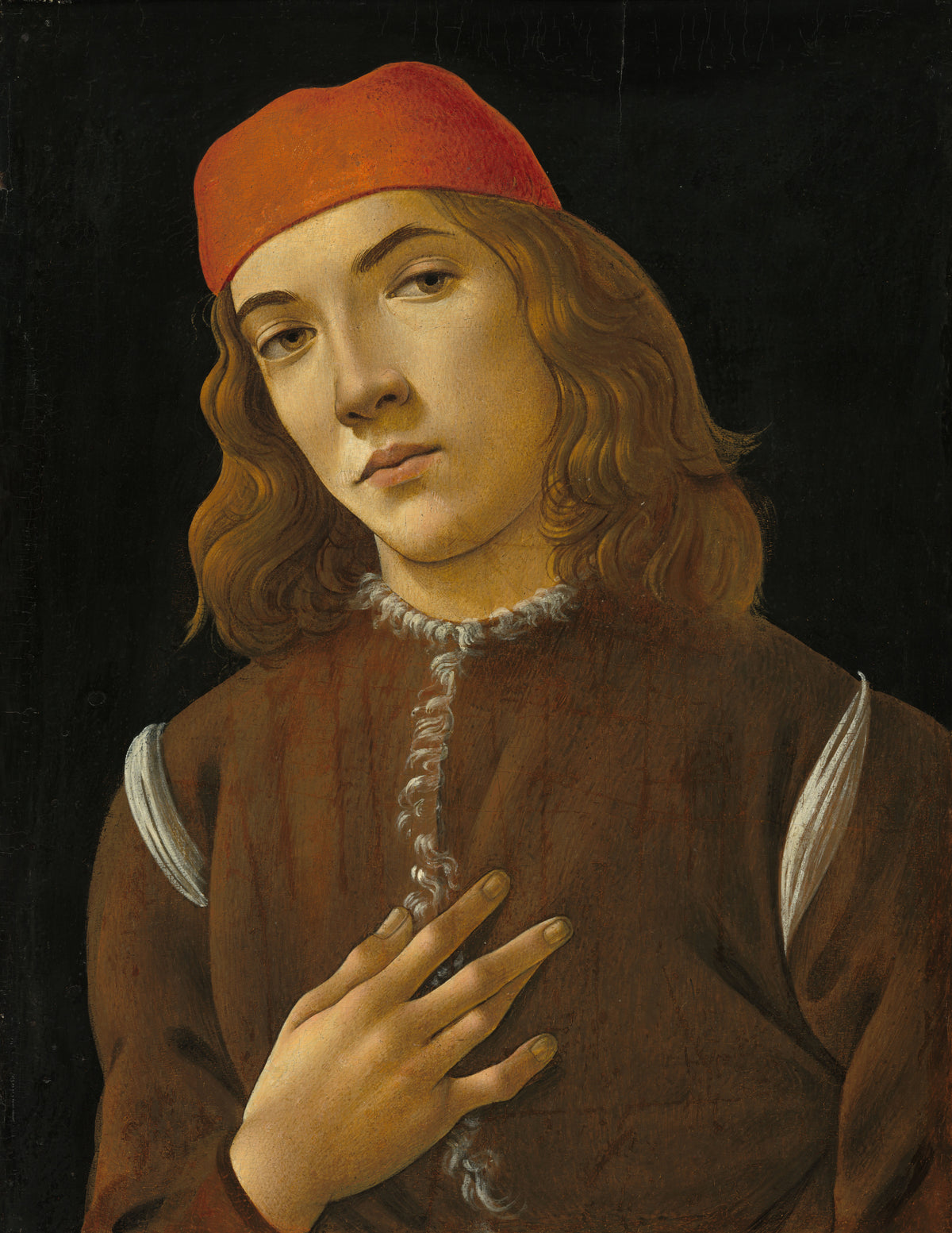 Portrait of a Youth by Sandro Botticelli — A red-capped youth with a hand on his chest against black