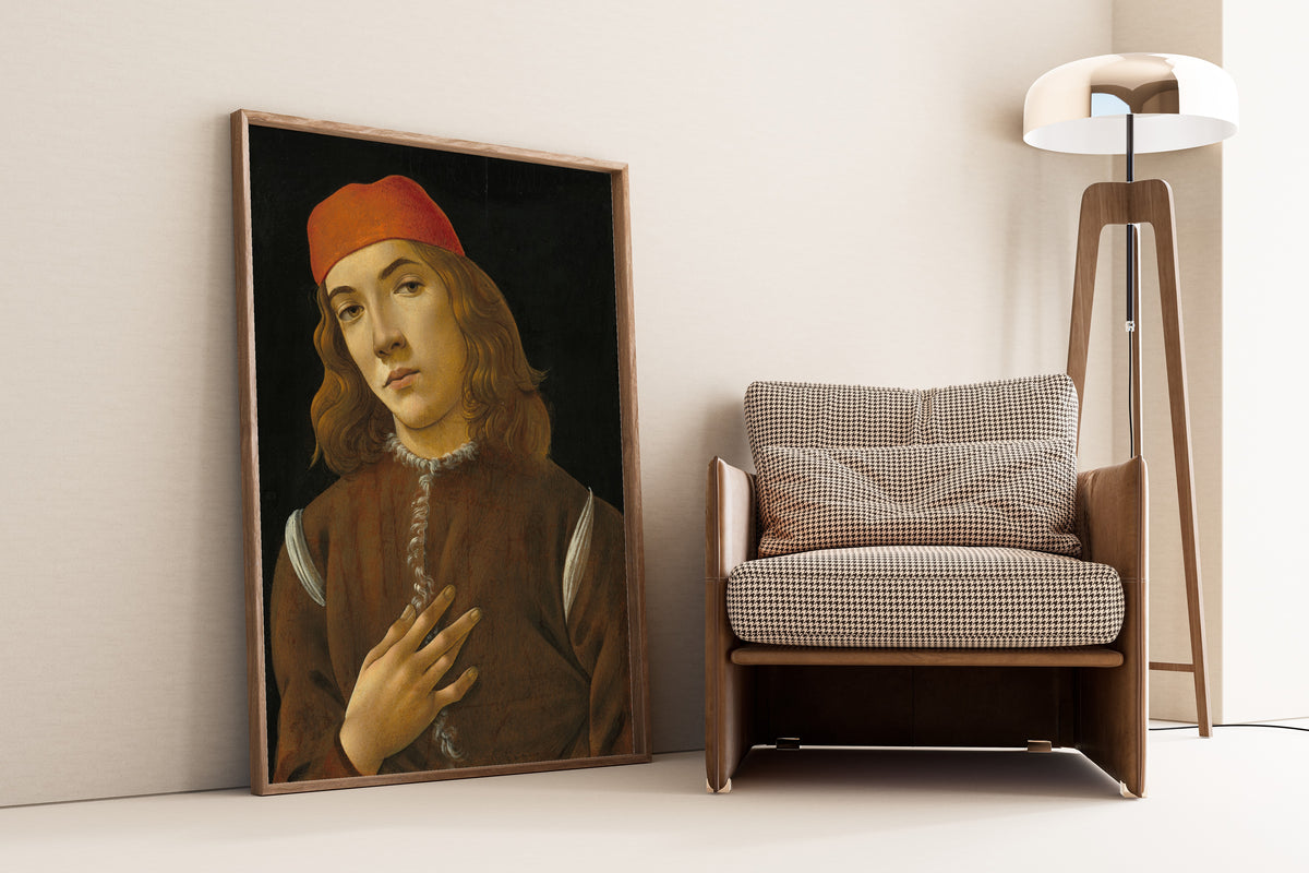 Framed art print of Portrait of a Youth by Sandro Botticelli, leaning against a wall beside an armchair and a floor lamp