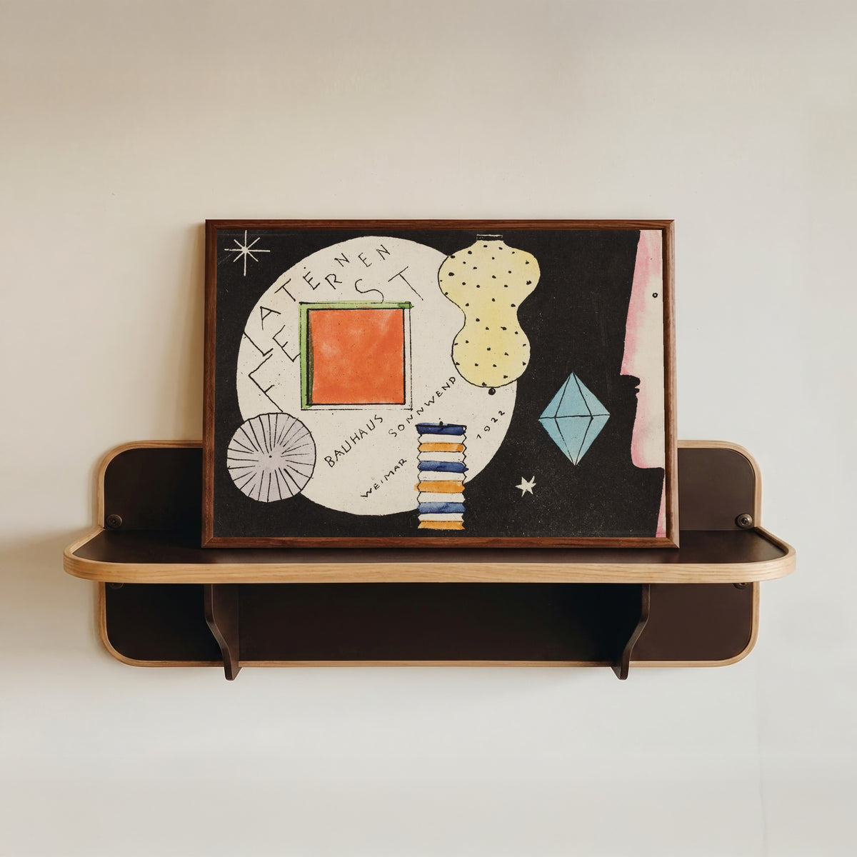 Framed art print of Postcard invitation to a lantern festival by Oskar Schlemmer, in a dark wood frame resting on a wall shelf