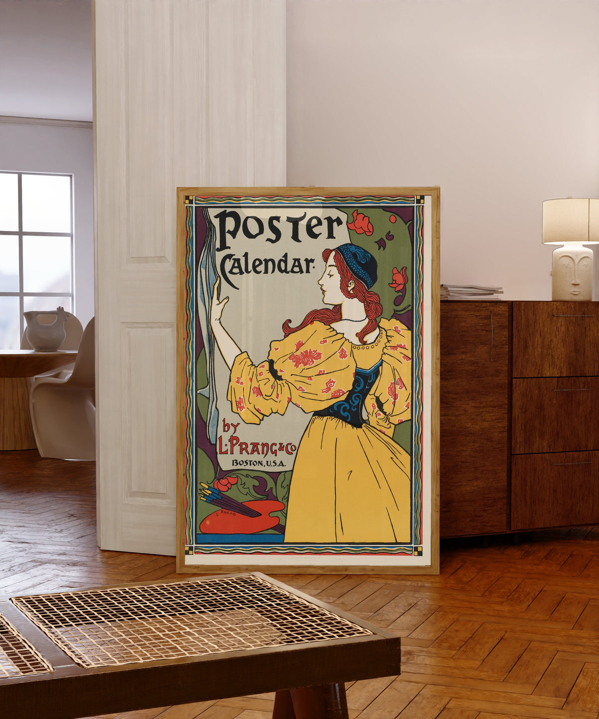 Framed art print of Poster Calendar by Louis Rhead, in a light wood frame leaning in a warm room with a parquet floor