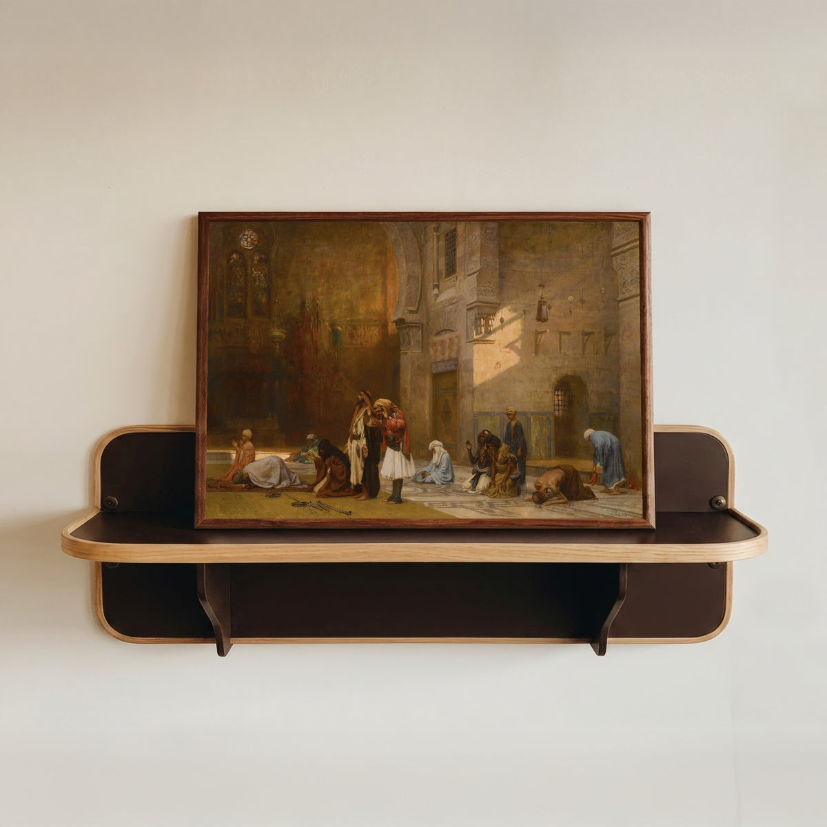 Framed art print of Prayer in the Mosque, Cairo by Frederick Arthur Bridgman, in a dark wood frame resting on a wall shelf