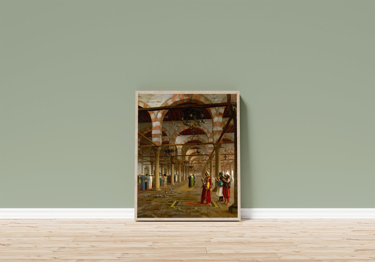 Framed art print of Prayer in the Mosque by Jean-Léon Gérôme, in a light wood frame leaning on a sage green wall above a wooden floor