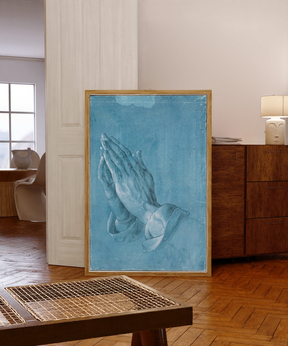 Framed art print of Praying Hands by Albrecht Dürer, in a light wood frame leaning in a warm room with a parquet floor