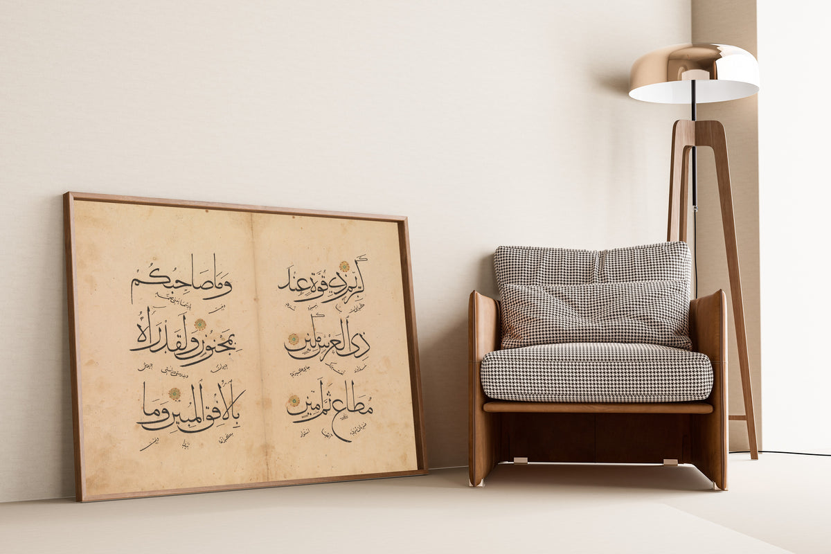 Framed art print of Qur'an Bifolium (Three Lines per Page), leaning against a wall beside an armchair and a floor lamp