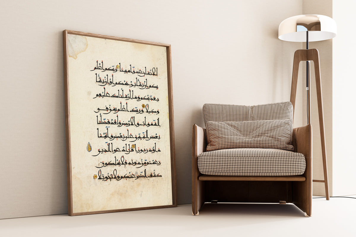 Framed art print of Qur'an Folio: Sura al-Isra', leaning against a wall beside an armchair and a floor lamp