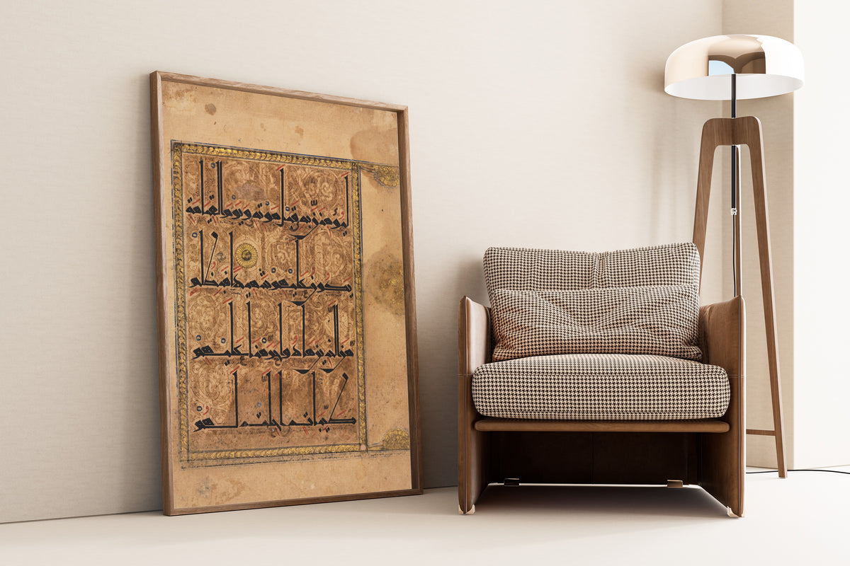 Framed art print of Qur'an Folio: Sura al-Nisa, leaning against a wall beside an armchair and a floor lamp