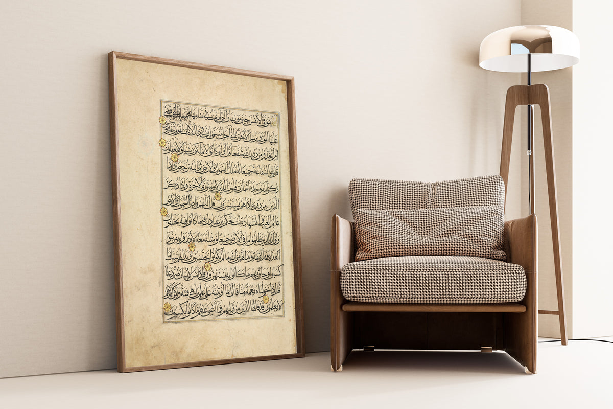 Framed art print of Qur'an Folio: Sura al-Zumar, leaning against a wall beside an armchair and a floor lamp