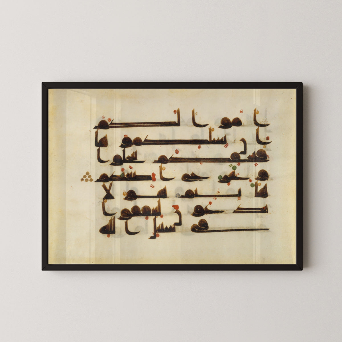 Framed art print of Qur'an Folio (Red and Green Dots on Parchment), in a black frame on a pale wall
